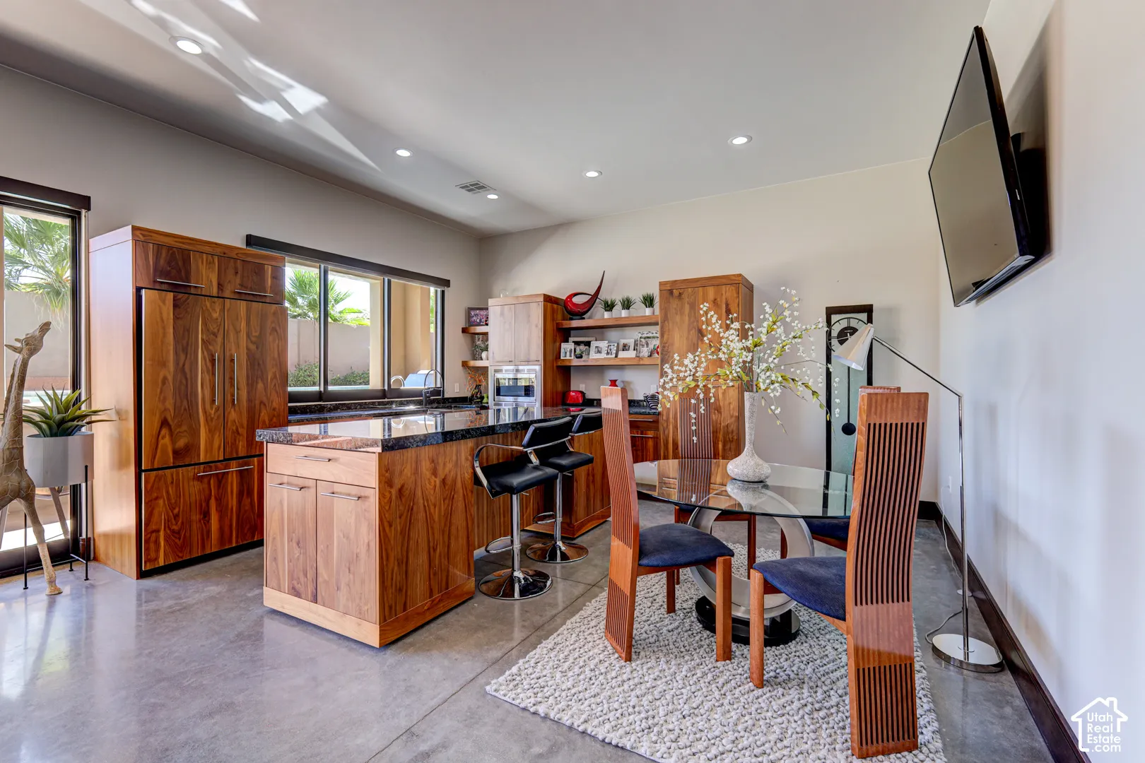 Integrated wood-finish paneled refrigerator, built-in cabinetry, polished concrete flooring, recessed lighting, and a wall-mounted flat-screen television