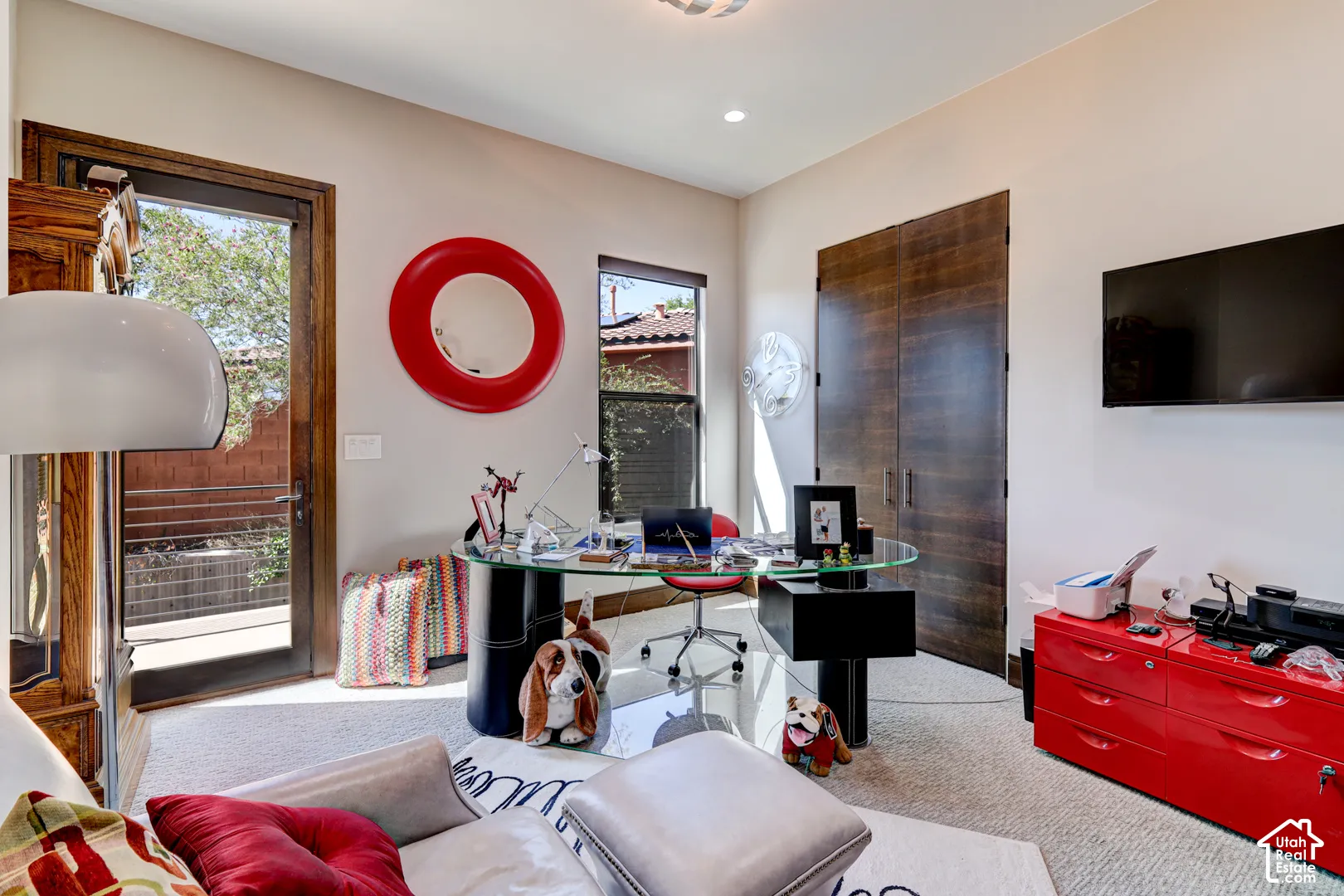 Recessed lighting, wood-finish double doors, a glass-top desk, a mounted television, and a glass-paneled exterior door