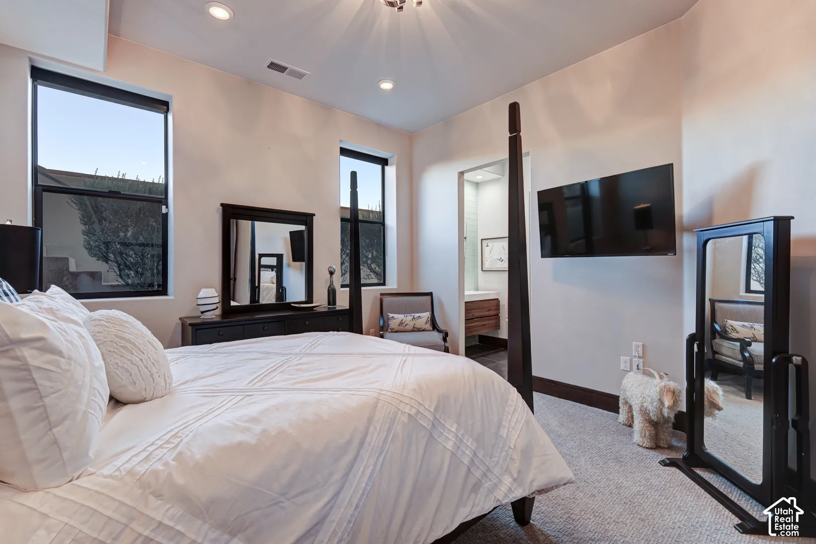 Recessed lighting and dual vertical windows illuminate this space, featuring carpet flooring and a wall-mounted flat-screen display