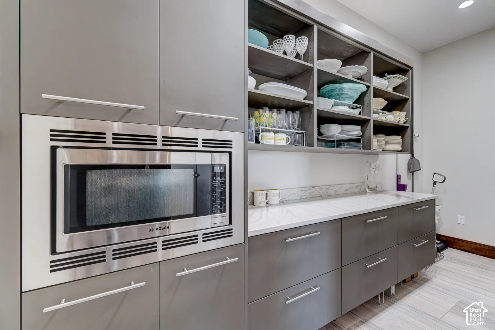 Built-in stainless steel microwave, extensive grey cabinetry, open shelving, light-toned countertop, and wood-finish flooring
