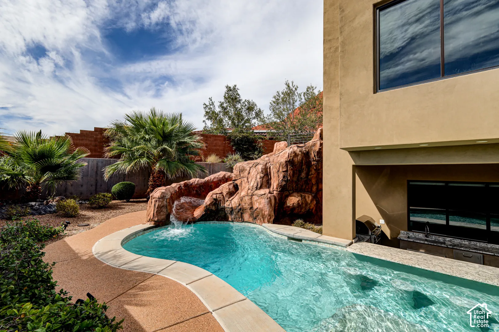 Curved pool with a rock waterfall feature, integrated submerged seating, and a perimeter pathway