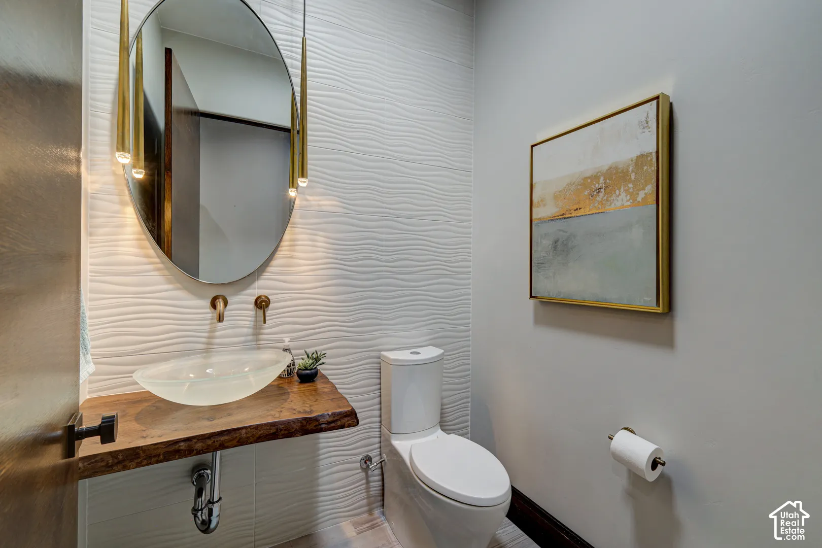 Textured accent wall, custom wood-slab vanity, vessel sink, wall-mounted faucet, and oval mirror with integrated lighting