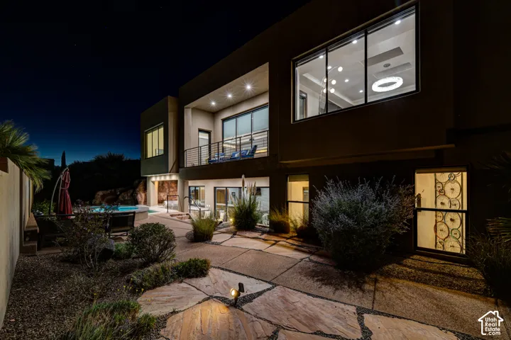 Multi-story exterior with a second-level balcony, ground-level patio with flagstone pavers, and an integrated pool area