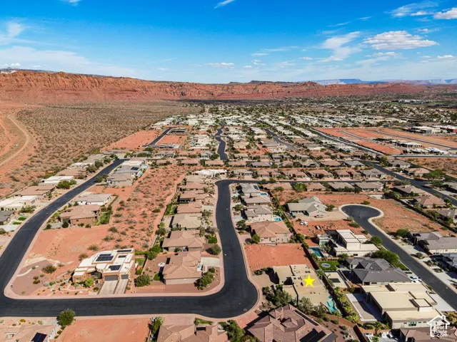 Aerial perspective showcasing residential properties and undeveloped lots with desert landscaping, surrounded by expansive red rock formations