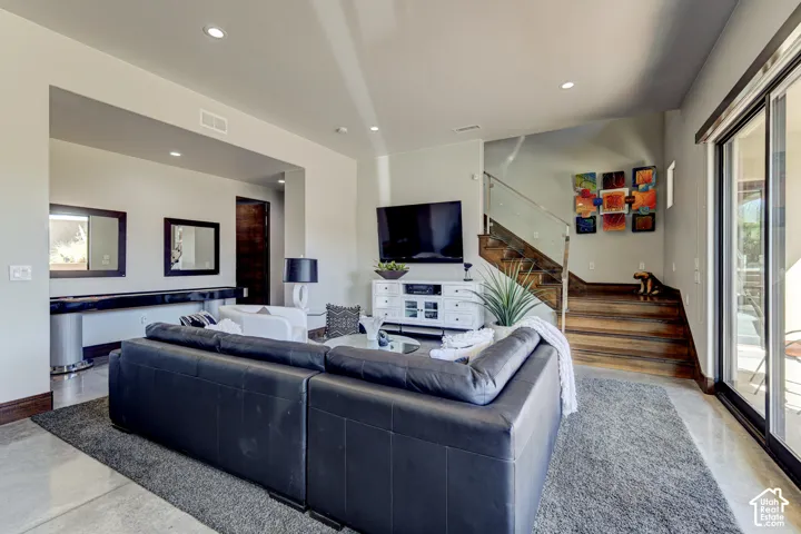 Recessed ceiling lighting, wood-finish flooring, sliding glass door, and a staircase with a glass and metal railing