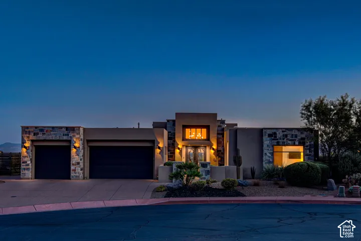 Architectural facade featuring stone accents, stucco finish, a two-car garage, desert landscaping, and a central entry with glass doors