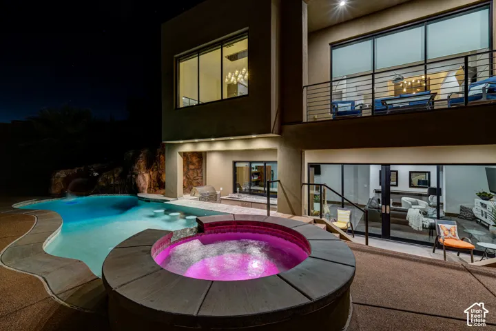 Multi-level modern exterior featuring a built-in spa, freeform swimming pool with rock waterfall, built-in outdoor kitchen, and a second-story balcony with metal railings