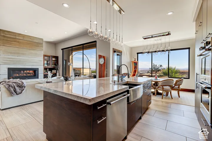 Open-concept living space featuring a linear fireplace, a kitchen island with a double basin farmhouse sink, wood-finish flooring, and expansive windows