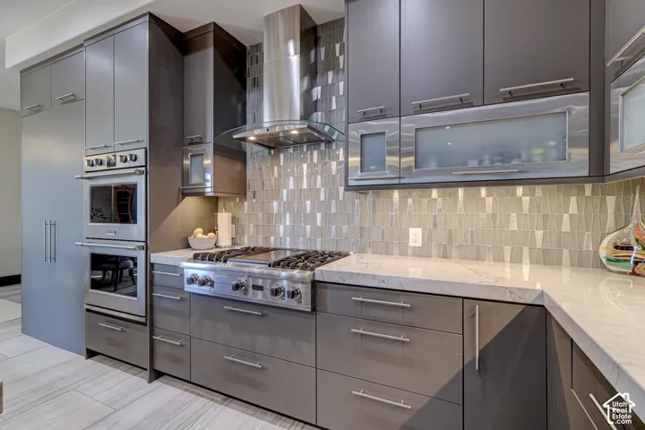 Contemporary kitchen featuring gray cabinetry, stainless steel appliances, a tile backsplash, and light-toned countertops