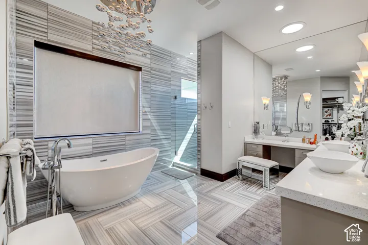 Freestanding bathtub with floor-mounted faucet, glass-enclosed shower, dual vanity with vessel sinks, and integrated lighting