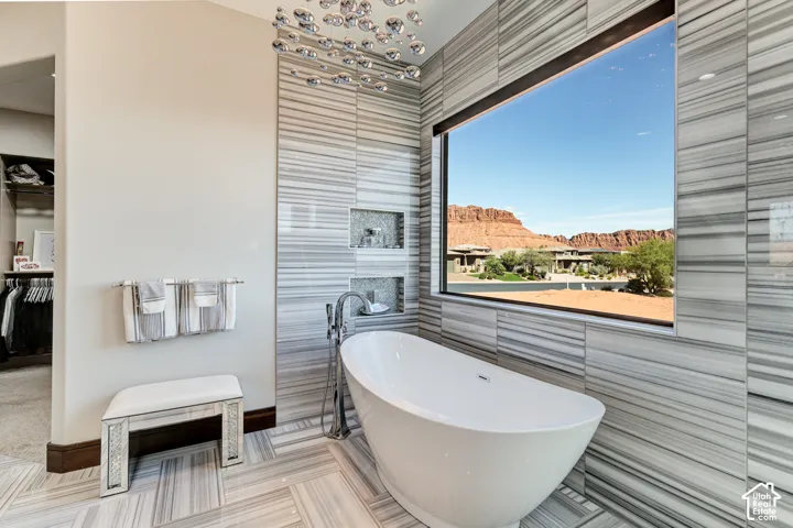 Freestanding soaking tub with floor-mounted faucet, striped tile surround, and large picture window
