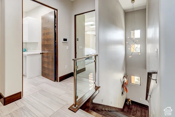 Multi-level interior featuring a contemporary chandelier, square wall windows, glass and metal railing, wood-finish flooring, and a solid wood door
