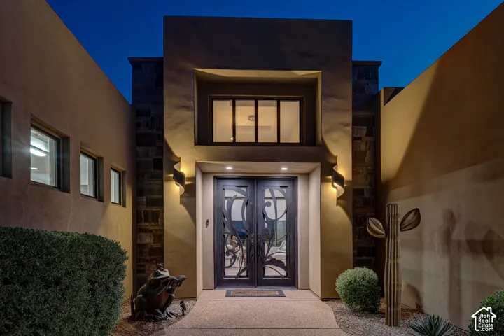 Stucco exterior with stone accents, illuminated entry, double doors with decorative glass, and upper level window