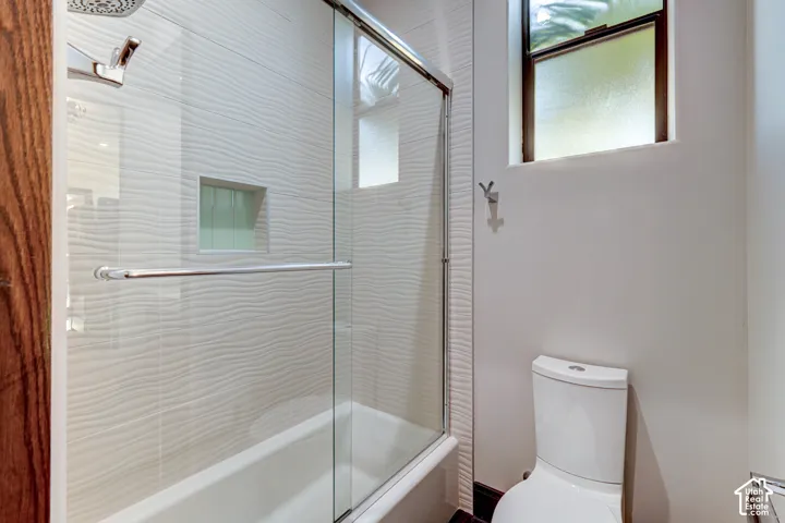 Bathtub with glass enclosure, textured tile surround, and a built-in shower niche