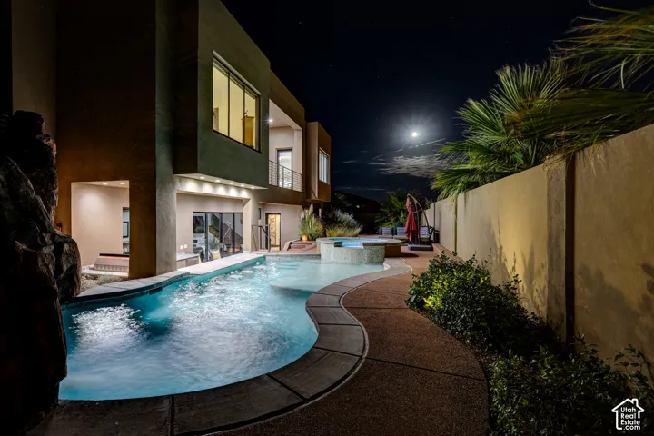 Curved swimming pool, integrated spa, adjacent hardscaping, and exterior lighting