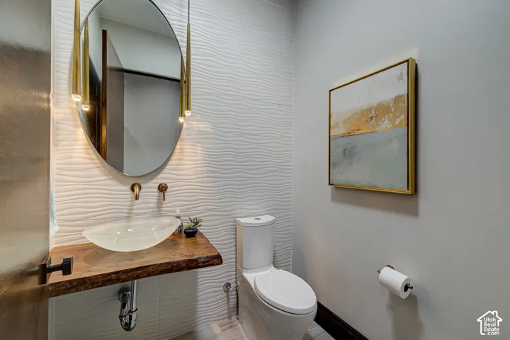Textured accent wall, custom wood-slab vanity, vessel sink, wall-mounted faucet, and oval mirror with integrated lighting
