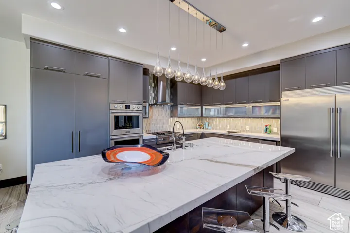Kitchen island with a waterfall edge, stone countertops, and recessed lighting