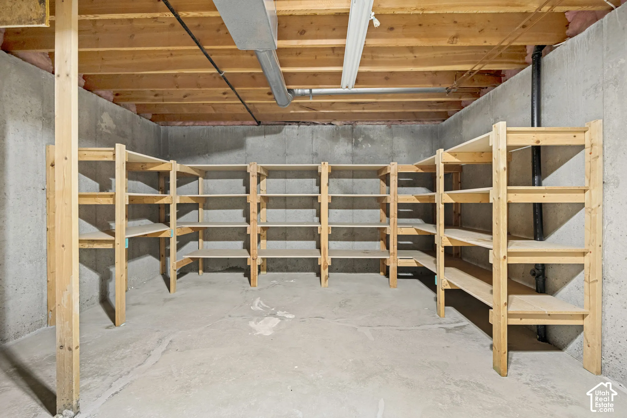 Basement storage area featuring extensive built-in wooden shelving, concrete walls, concrete flooring, and exposed ceiling joists
