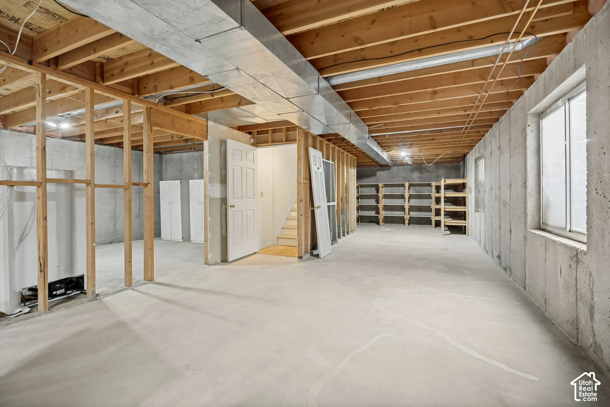 Unfinished basement with concrete flooring, exposed wood joists, framed walls, and multiple windows