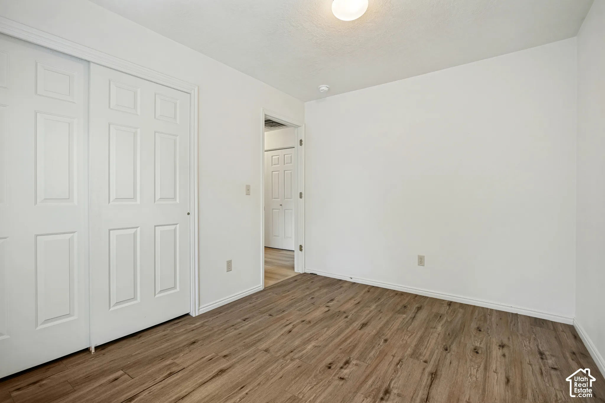 Wood-finish flooring, white walls, and a flush-mount ceiling light