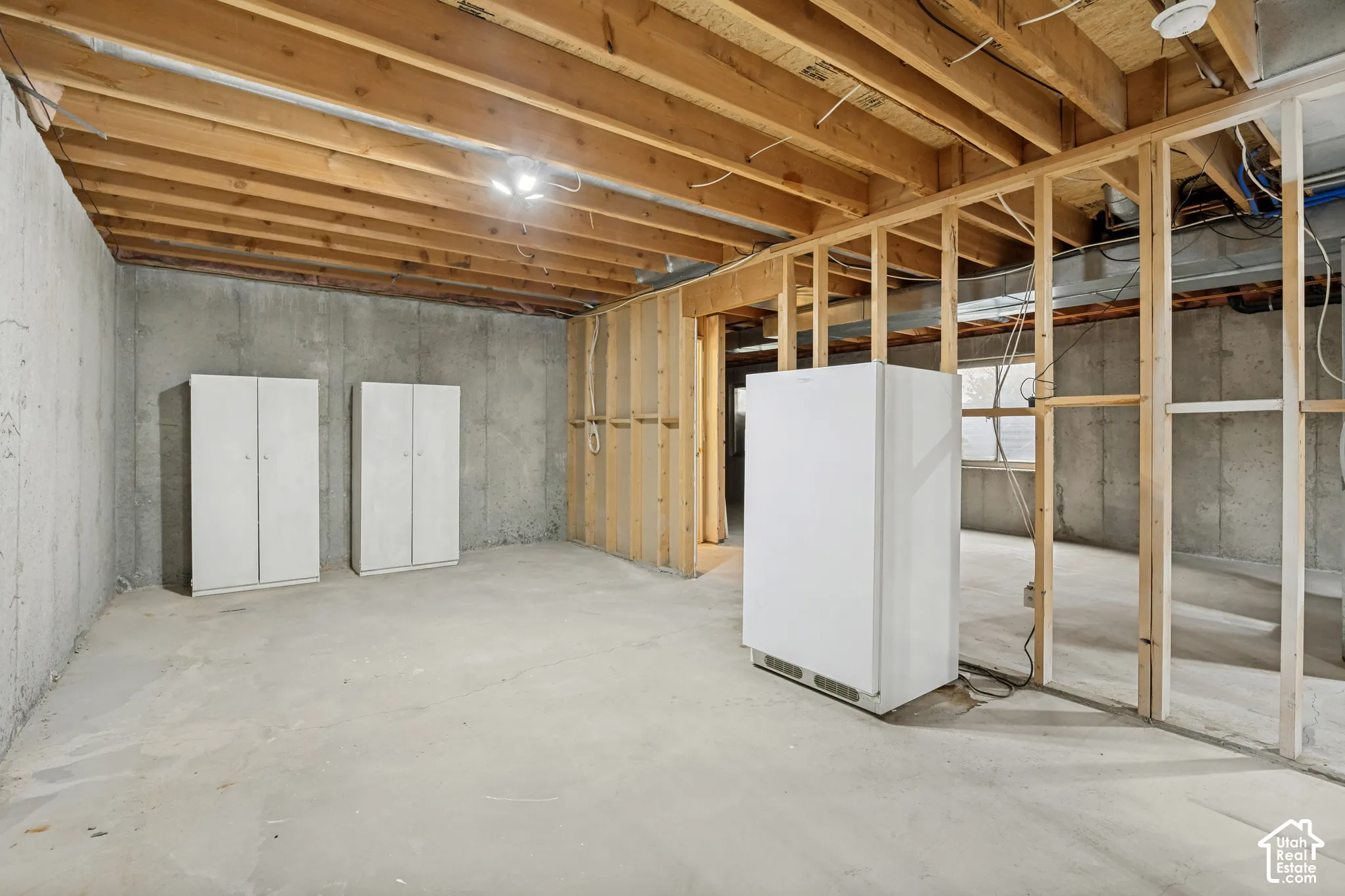 Unfinished basement space featuring exposed wooden ceiling joists, concrete flooring, concrete walls, and framed interior partitions