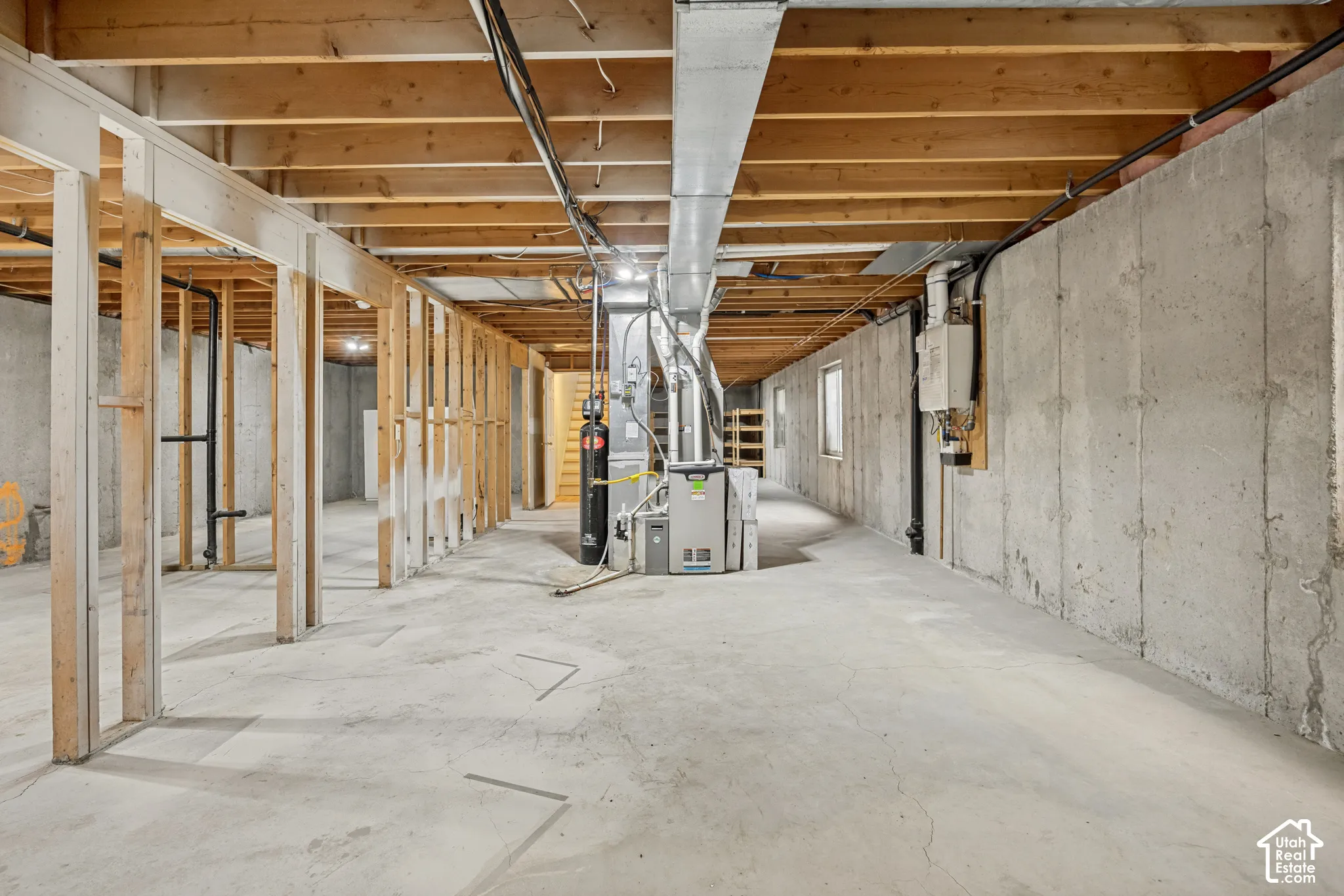Unfinished basement featuring concrete flooring, exposed wood joists, framed partition walls, and mechanical systems