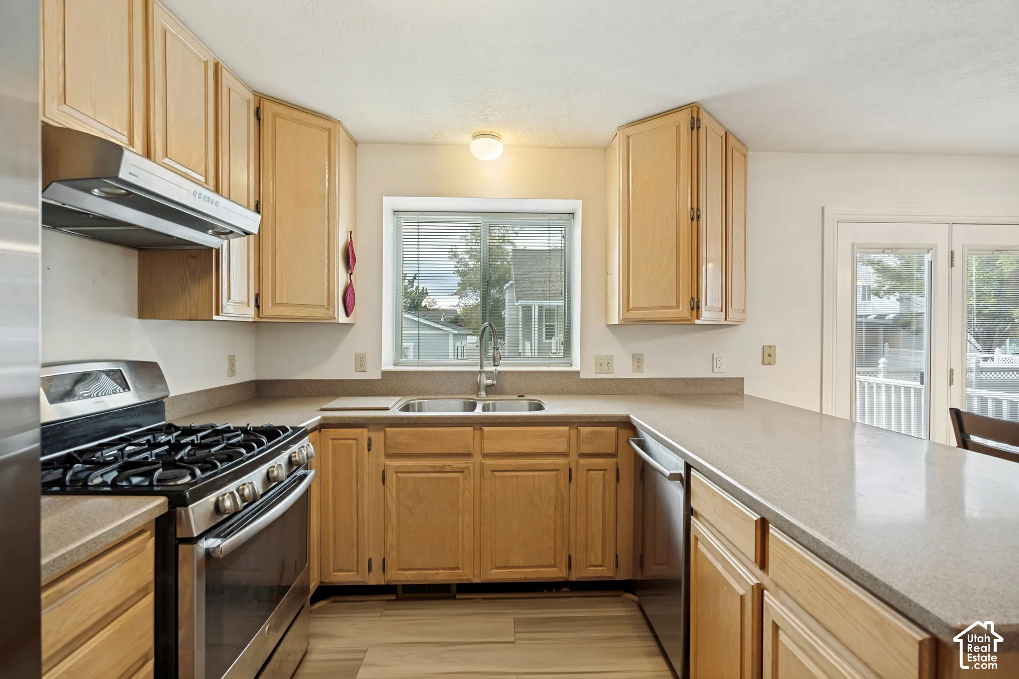 Kitchen featuring light wood cabinetry, a stainless steel gas range with a matching range hood, and a built-in dishwasher