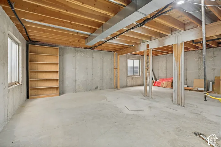 Concrete flooring, exposed wood ceiling joists, concrete walls, multiple windows, built-in shelving unit