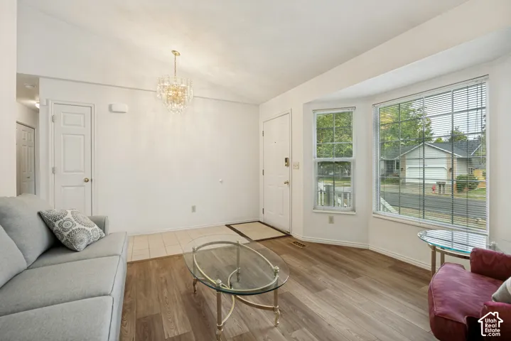 Vaulted ceiling with a chandelier, wood-finish flooring, bay windows, and a tiled entry
