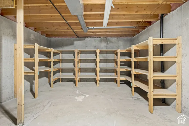 Basement storage area featuring extensive built-in wooden shelving, concrete walls, concrete flooring, and exposed ceiling joists