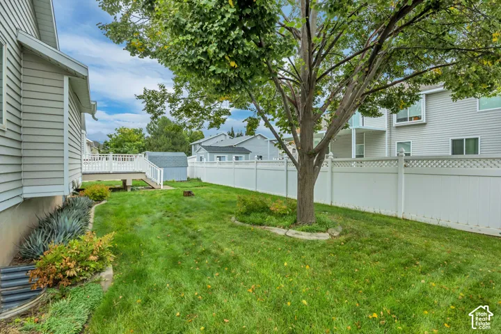 Expansive rear yard featuring a manicured lawn, established tree, and white privacy fencing