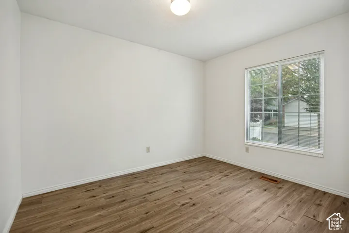 Light wood-finish flooring, white walls, and a large window with white blinds