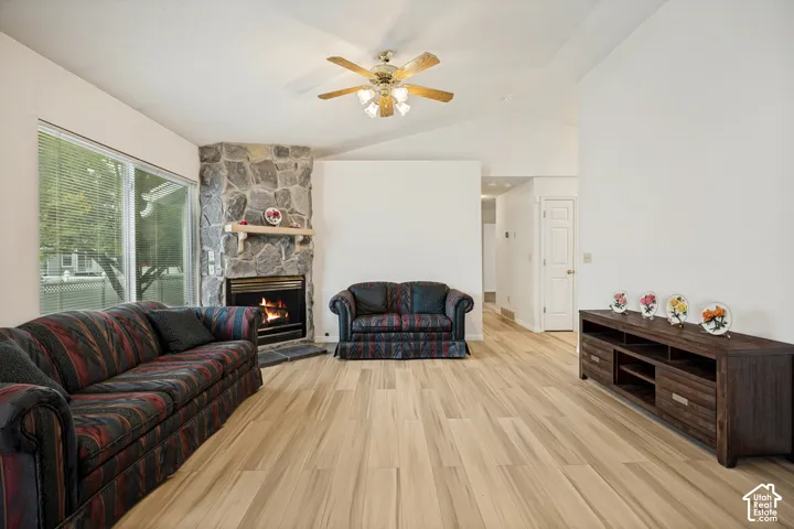 Vaulted ceiling, stone-clad fireplace, wood-finish flooring, ceiling fan, and large windows