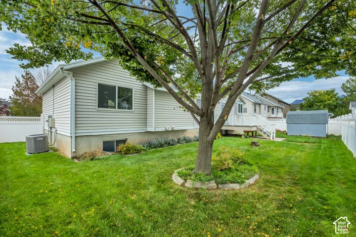 Expansive grassy yard featuring a large mature tree, a white vinyl fence, and a storage shed