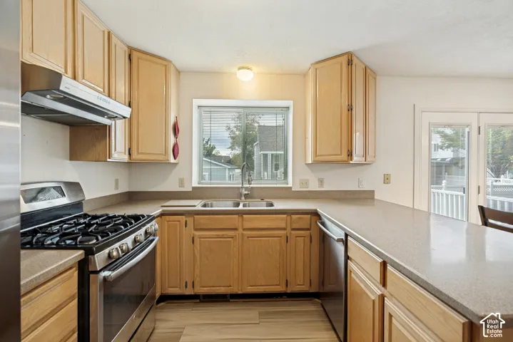 Kitchen featuring light wood cabinetry, a stainless steel gas range with a matching range hood, and a built-in dishwasher