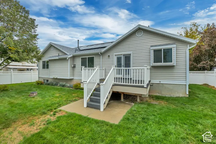 Rear exterior featuring light-toned siding, a deck with white railings, and a concrete patio