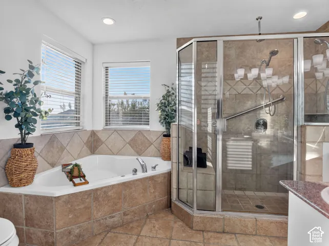 Corner soaking tub with tile surround, adjacent glass-enclosed shower, and dual windows with blinds