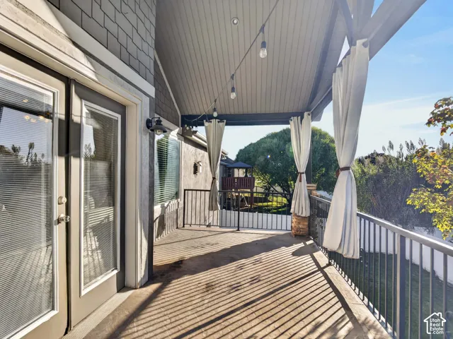 Covered outdoor deck with exposed beam ceiling, string lighting, and black metal railing
