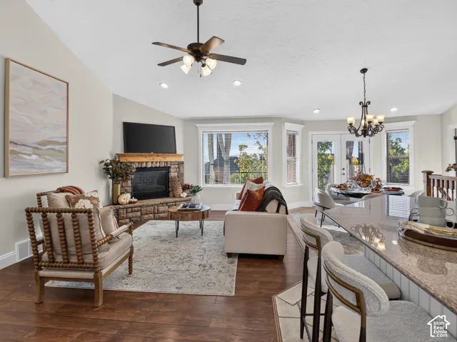 Vaulted ceiling featuring a ceiling fan, stone-surround fireplace with wood mantel, wood-finish flooring, bay windows, and a raised countertop with bar seating