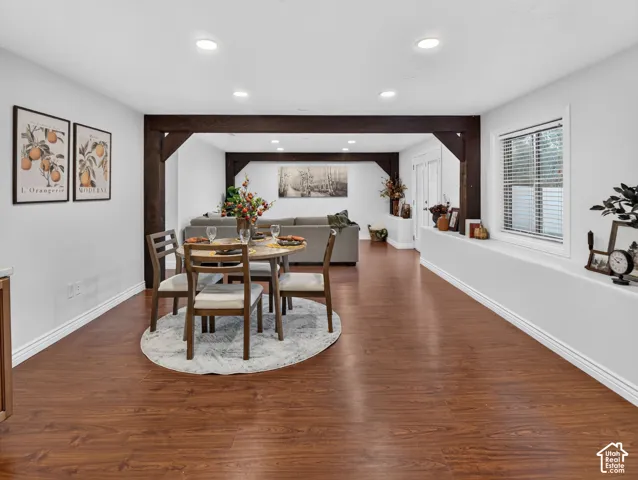 Spacious open-concept dining and living area featuring rich wood-finish flooring, recessed ceiling lighting, and an arched architectural entry with dark wood framing