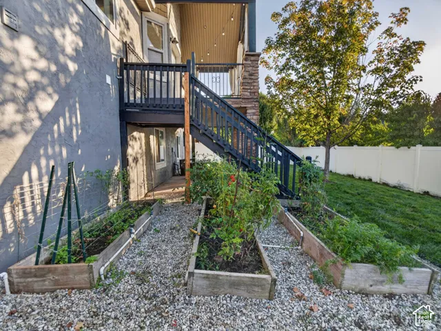 Raised garden beds, gravel ground cover, exterior staircase with dark railing, stone column accent, and a privacy fence