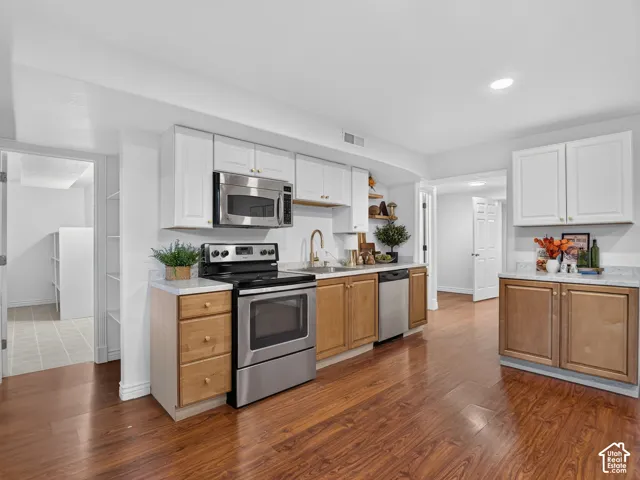 Basement kitchen featuring wood-finish flooring, white upper cabinetry, natural wood-tone lower cabinetry, stainless steel appliances, and light-toned countertops