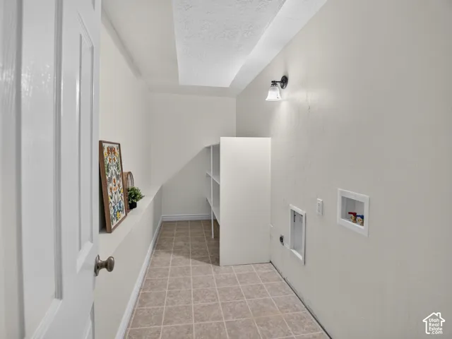 Basement laundry area featuring durable tile flooring, built-in shelving, sconce lighting, and utility hookups