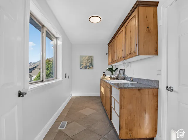 Built-in wood cabinetry with a natural finish, stone countertop with integrated sink, and tiled flooring