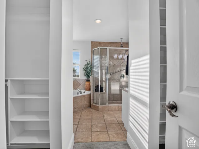 Built-in shelving, corner soaking tub, glass-enclosed shower, tiled flooring, and tiled shower surround