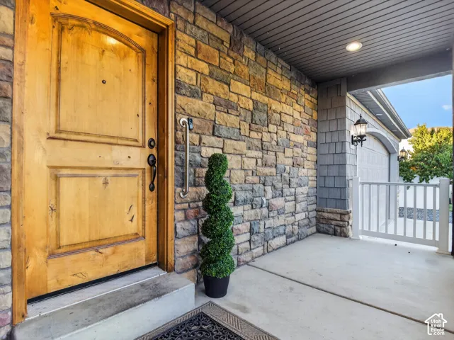 Stone accent wall, wood-paneled entry door, recessed ceiling light, shaker shingle siding, and large concrete porch