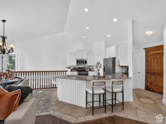 Vaulted ceilings with recessed lighting, white cabinetry, stainless steel appliances, and a wood-finish entry door
