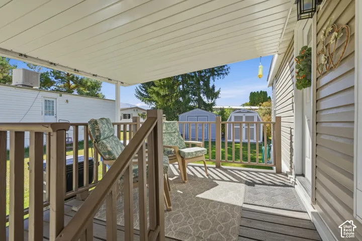 Covered porch with wood-finish decking, tan siding, and black outdoor sconce
