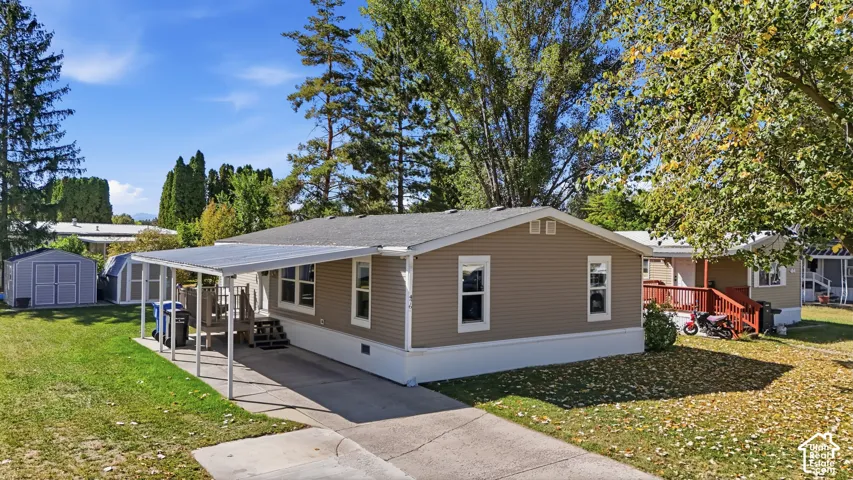 Tan siding exterior with white trim, covered carport, gravel driveway, and two storage sheds
