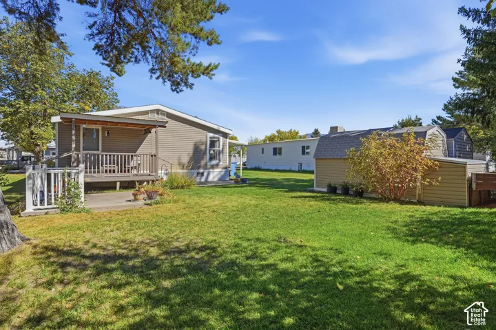 Expansive green lawn with mature trees, covered porch with wood railing, paved patio area, and an accessory building with a gambrel roof
